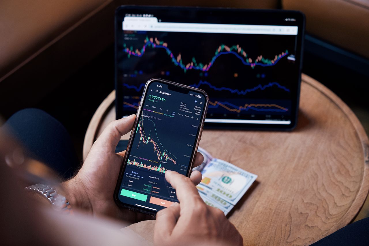 Close-up of someone trading stocks with a smartphone and a tablet.